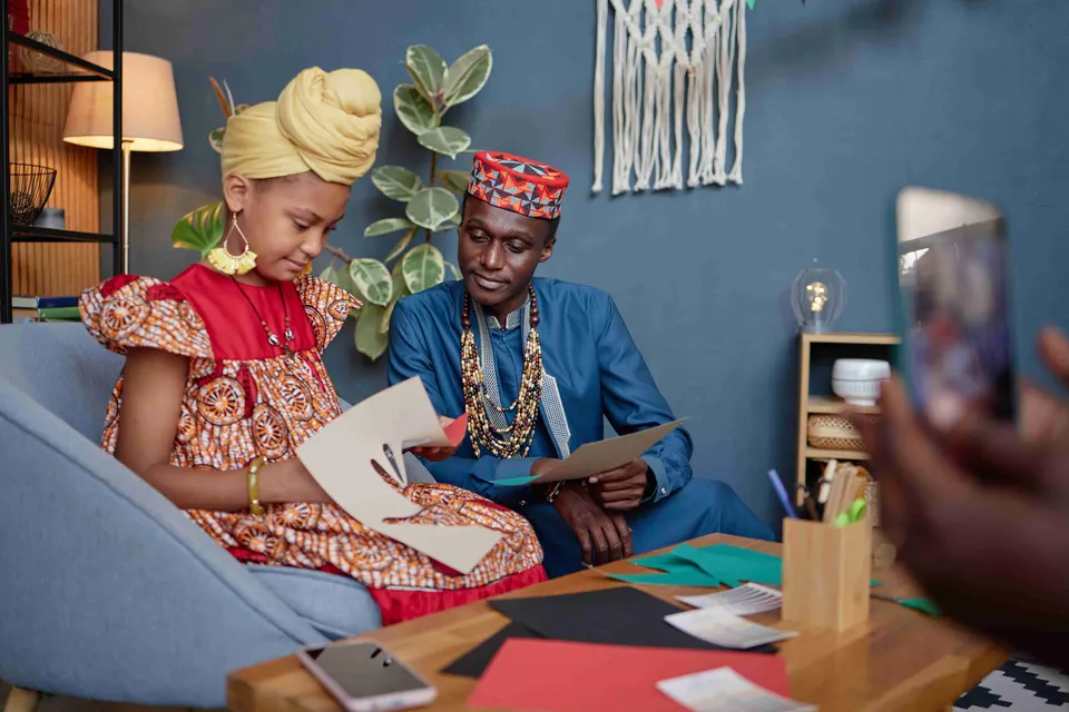 Father and daughter in African-print outfits working through a lesson at home