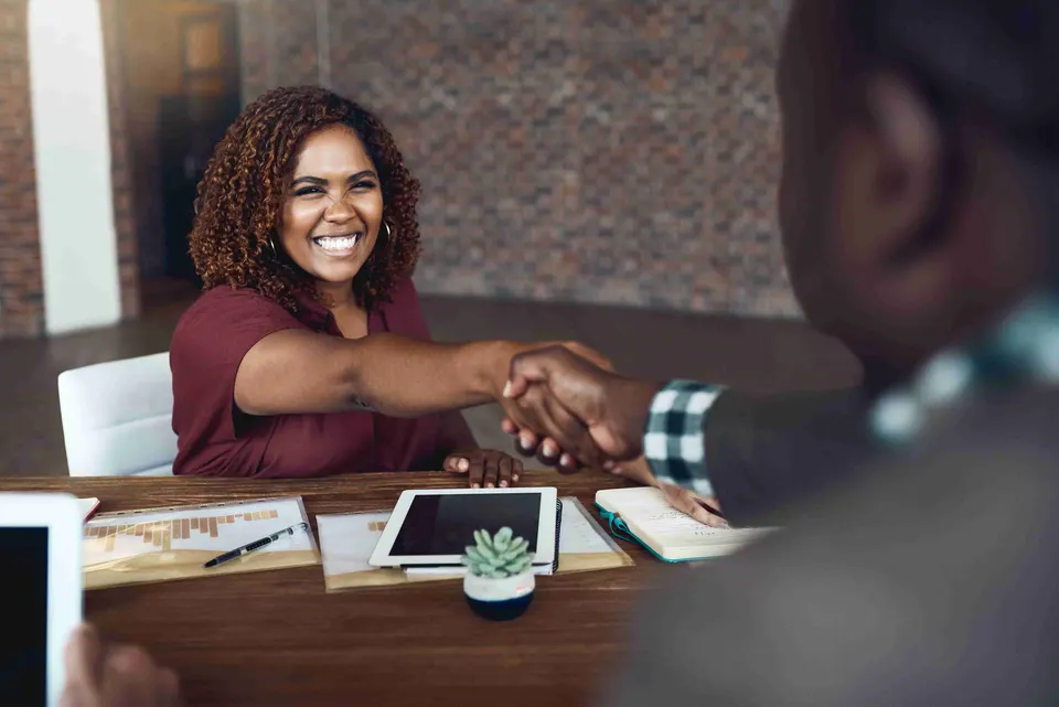 Smiling woman shaking hands across a desk in an office meeting