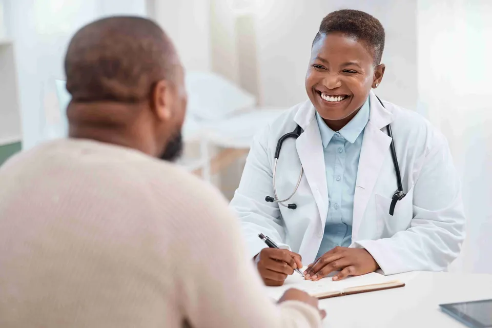 Smiling doctor writing notes while talking with a patient